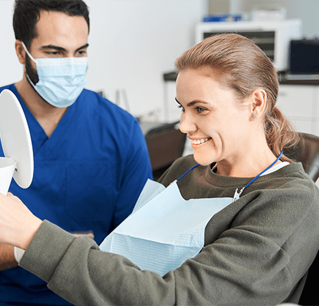 Woman looking at her smile in a mirror at the dentist.